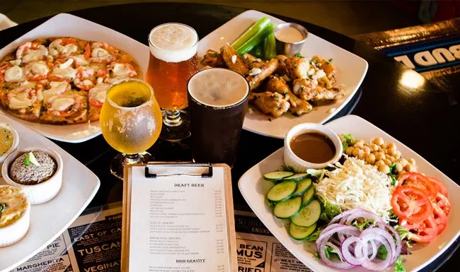 Overhead view: Beer, pizza, wings, salad, and dips on dark table.