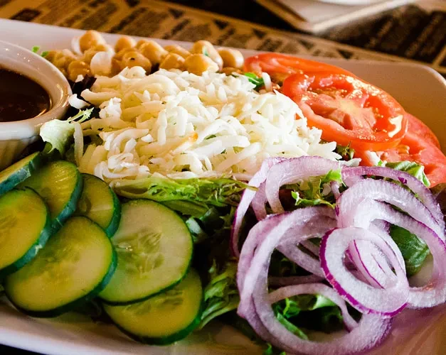 Close-up, colorful salad with tomatoes, cucumber, red onion, cheese, and dressing.
