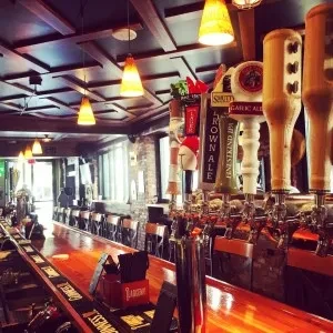 Polished wooden bar counter with numerous beer taps and empty stools.