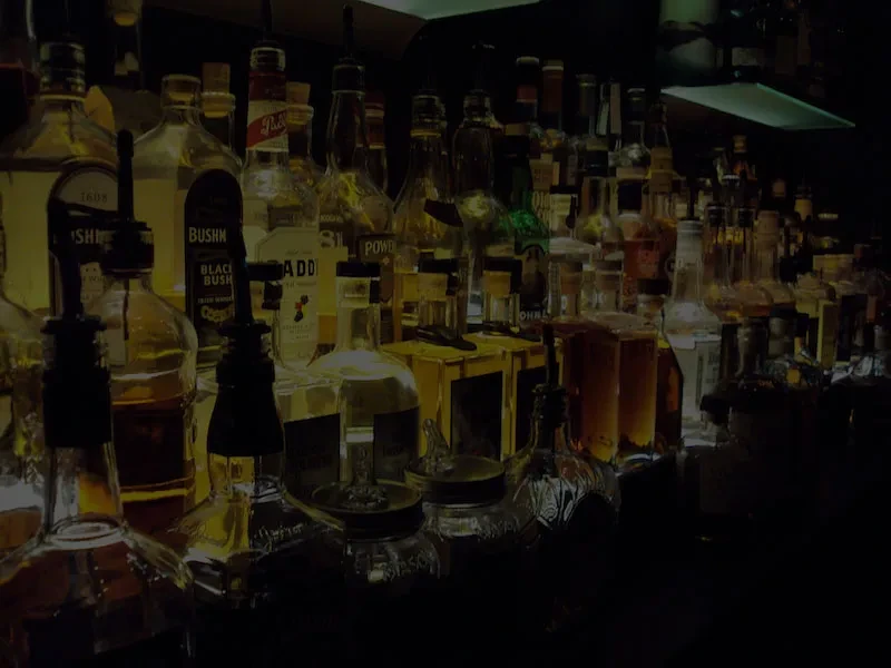 Shelves of liquor bottles shine with a golden glow in a dark bar.