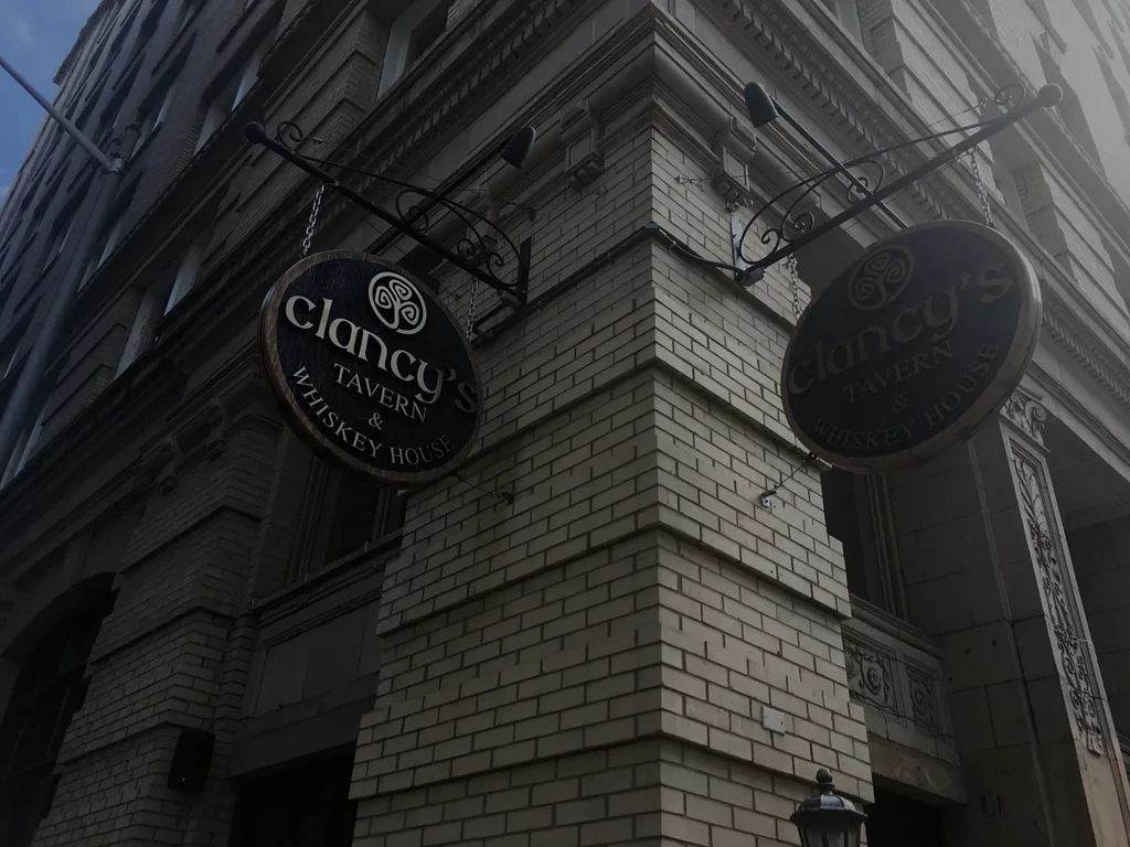 Upward view of Clancy's Tavern brick building with ornate hanging signs.