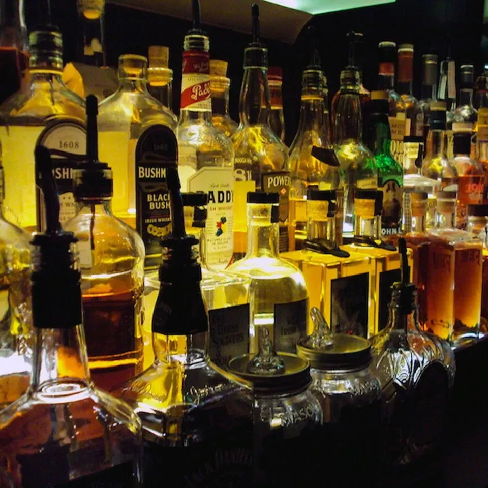 Warmly lit bar shelf stocked with numerous liquor bottles.