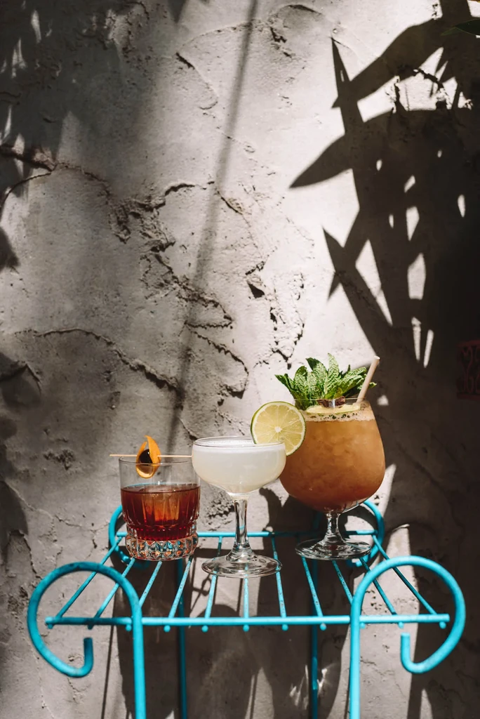 Three distinct cocktails on a vibrant blue shelf with dramatic shadows.