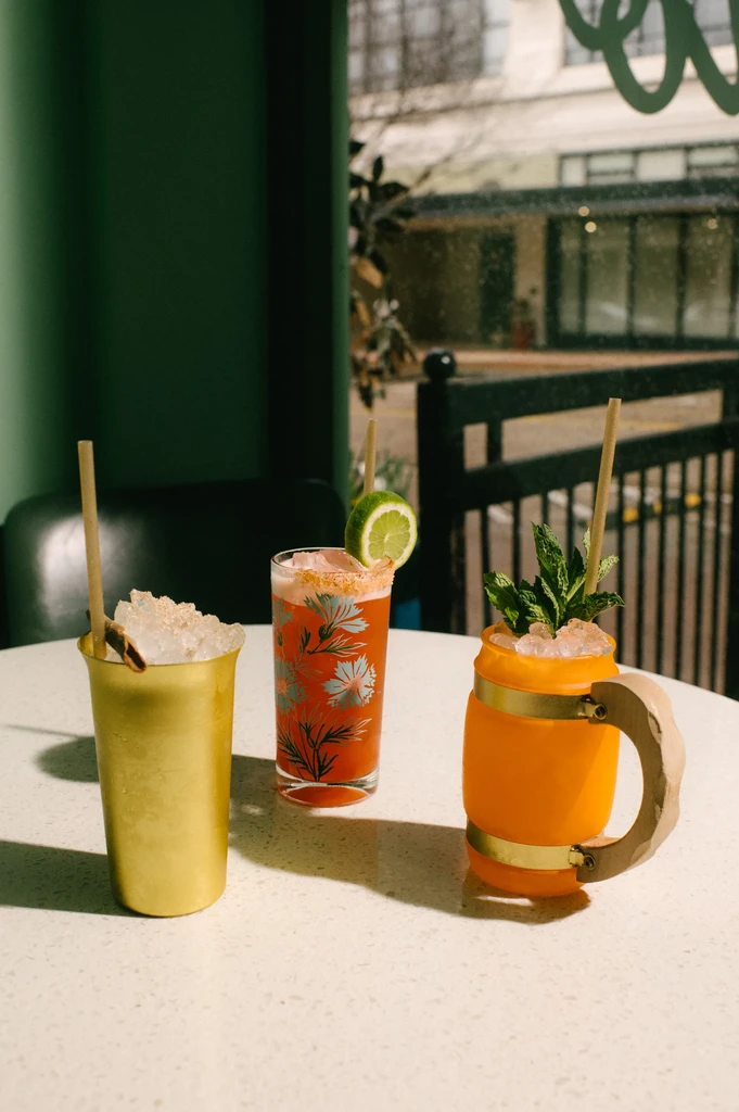 Colorful, elaborate cocktails on a bright table with a blurred city view.