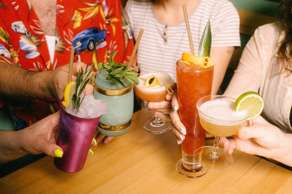 Five distinct, elaborately garnished cocktails held by several people.