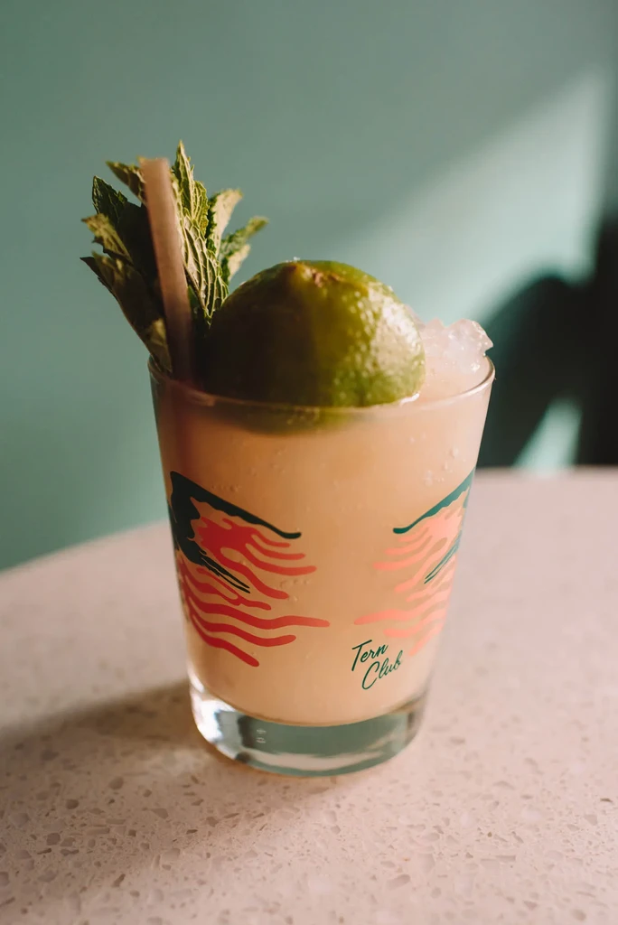 Close-up of a cocktail with lime, mint, crushed ice, and 'Tern Club' glass.