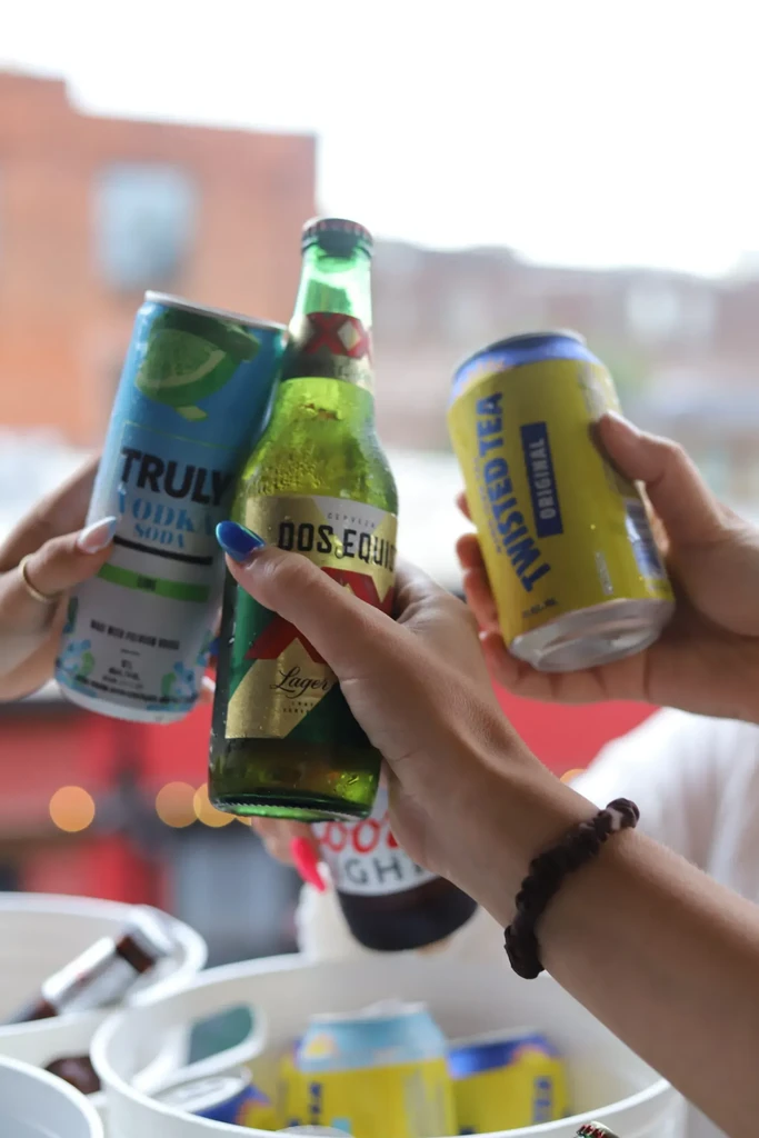 Three hands hold Truly, Dos Equis, and Twisted Tea in a toast.