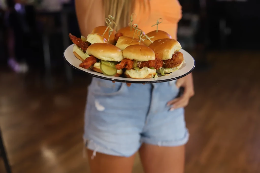 Person holds a plate of six fried chicken sliders with pickles.
