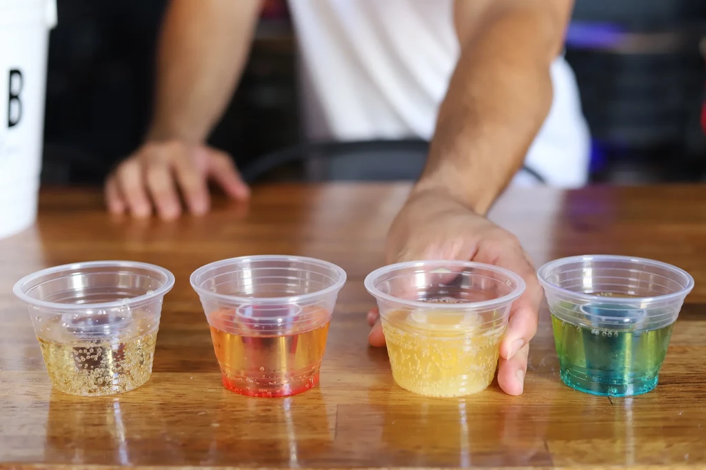 Four colorful layered drinks with nested shot glasses on a wooden table.