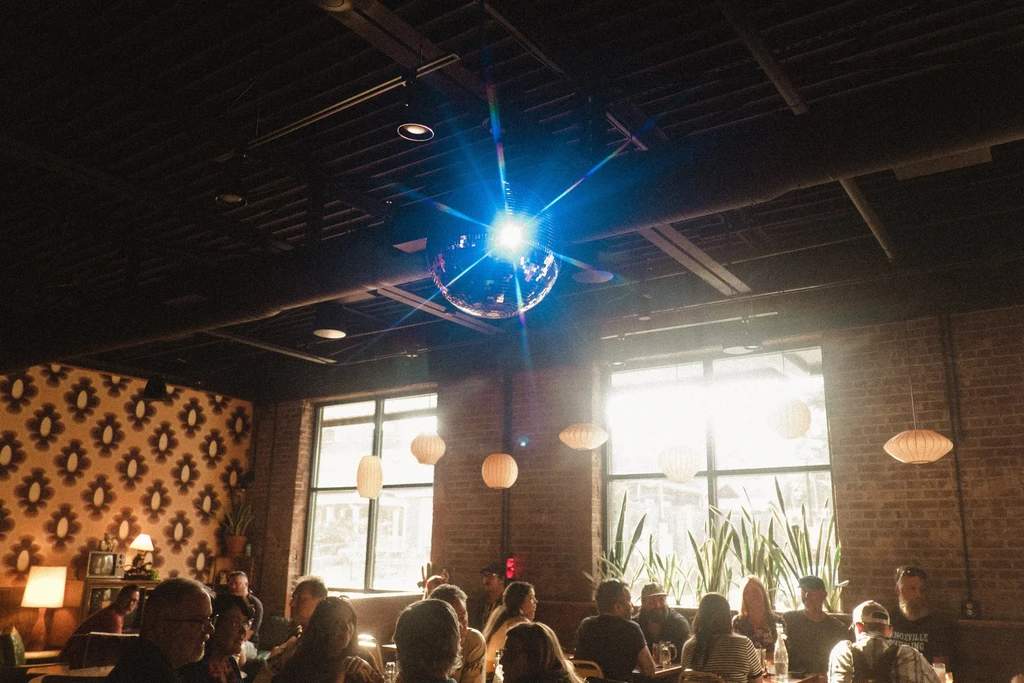 Lively, retro bar interior with a blue disco ball and patrons.