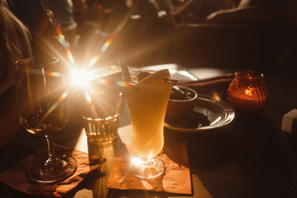 Dimly lit table with cocktail, glasses, and glowing candle, strong lens flare.