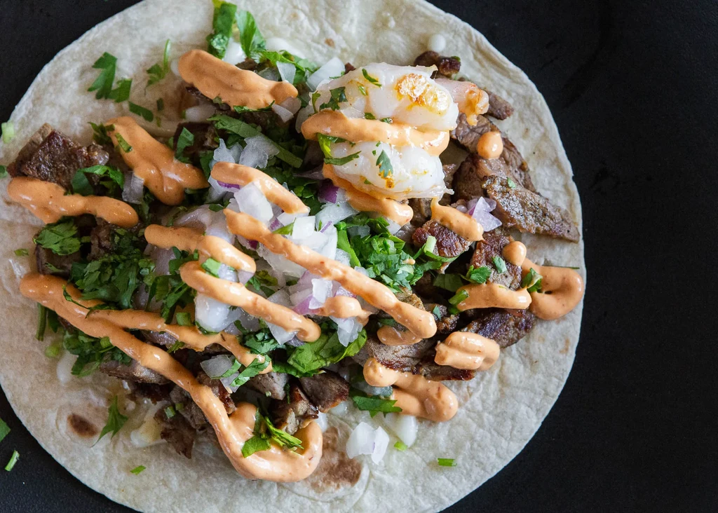 Close-up, top-down view of a shrimp and steak taco with sauce.