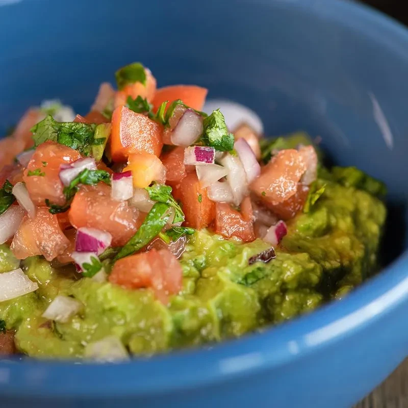 Chunky guacamole topped with fresh pico de gallo in a blue bowl.