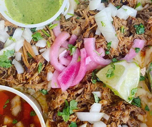 Colorful shredded meat tacos with pickled onions, cilantro, lime, and salsas.