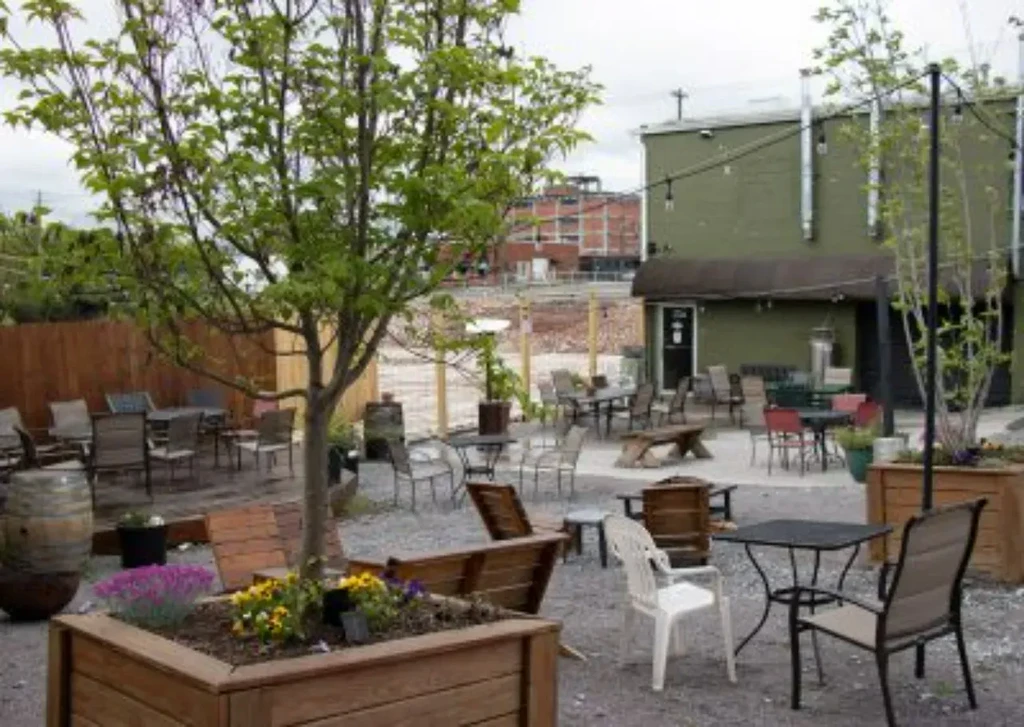 Rustic outdoor restaurant patio with varied seating, trees, and string lights.