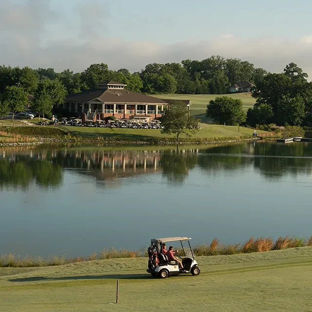 Golf course clubhouse reflecting in lake, many parked golf carts.