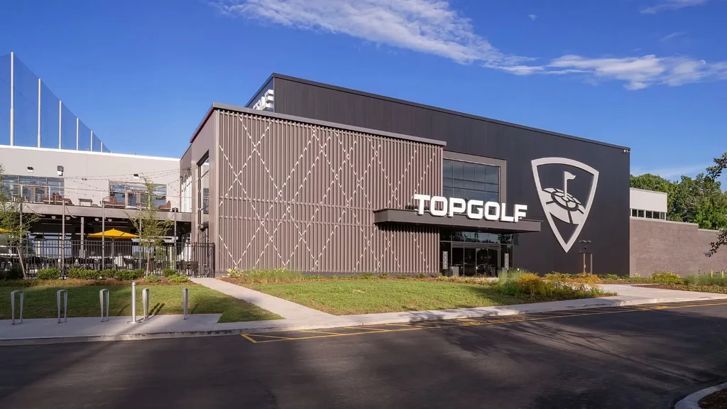 Modern Topgolf facility with multi-level building, patio, and golf netting.