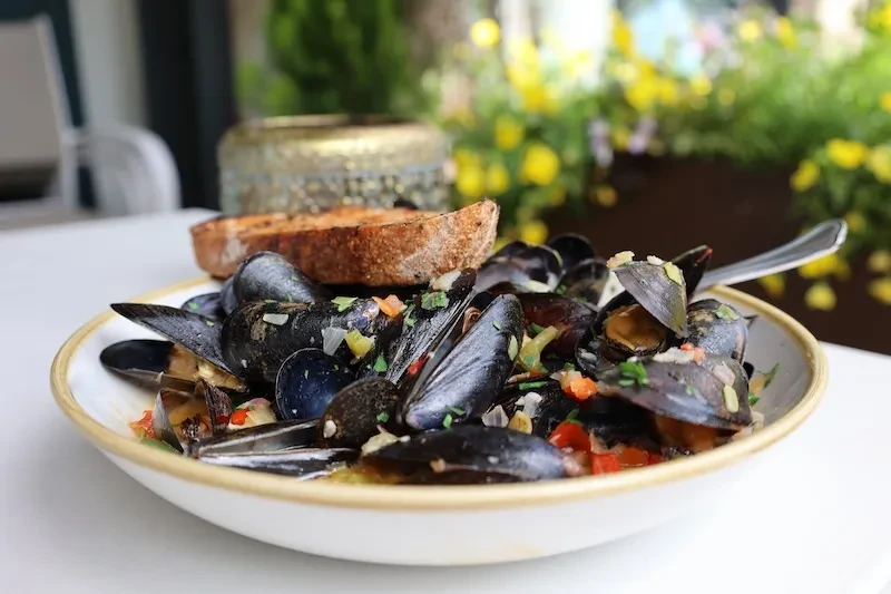 Steamed mussels with vegetables, rustic bread, and a spoon.