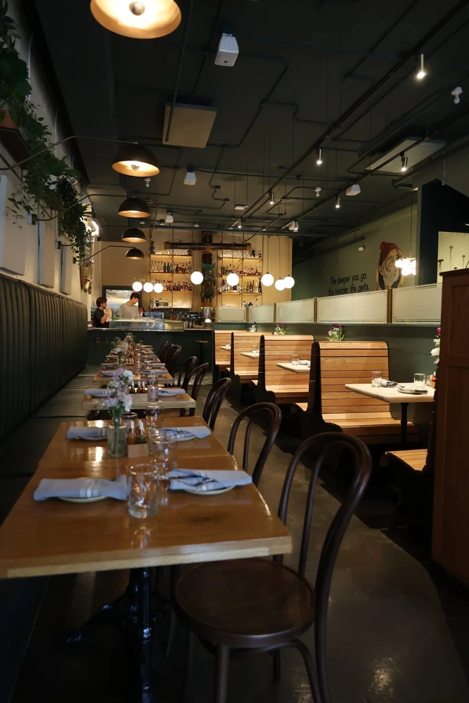 Industrial-style restaurant with long aisle of dining tables and bar.