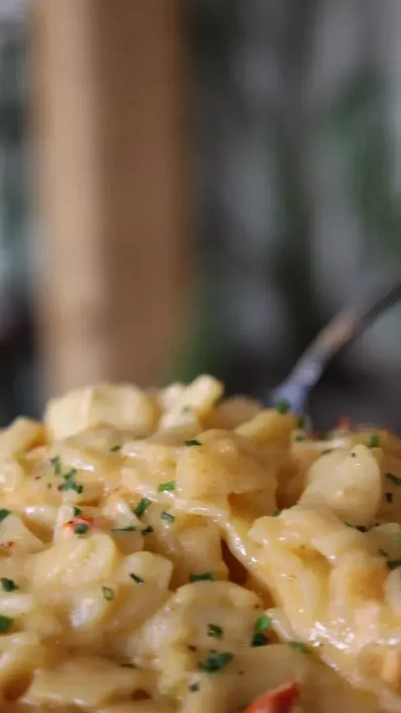 Close-up of cheesy pasta with green herbs and red spices, a fork visible.
