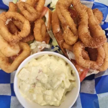 Fried calamari rings, lettuce, tomato, and potato salad in a checkered liner.