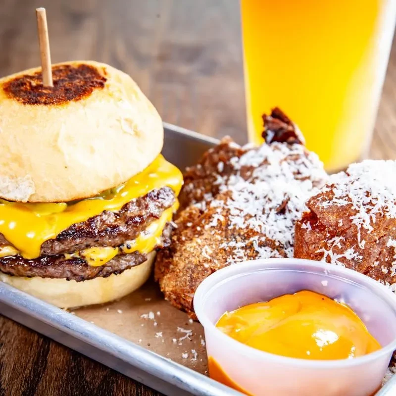 Double cheeseburger, fried items with white flakes, and orange sauce on a tray.