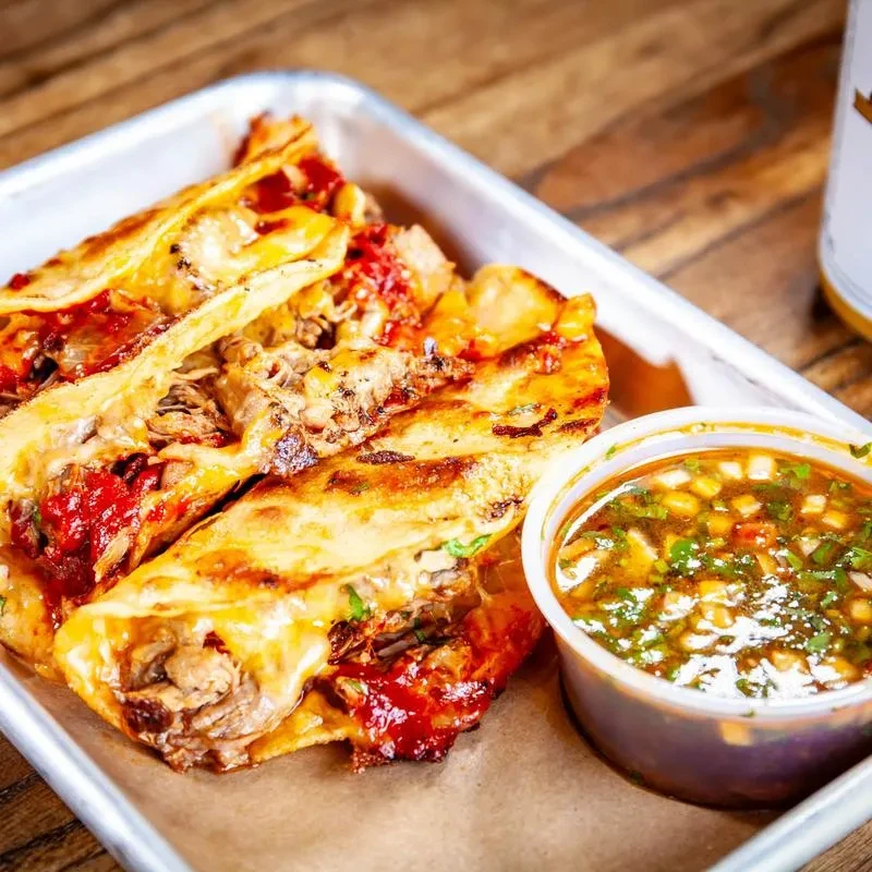 Three grilled meat and cheese tacos with green dipping sauce.
