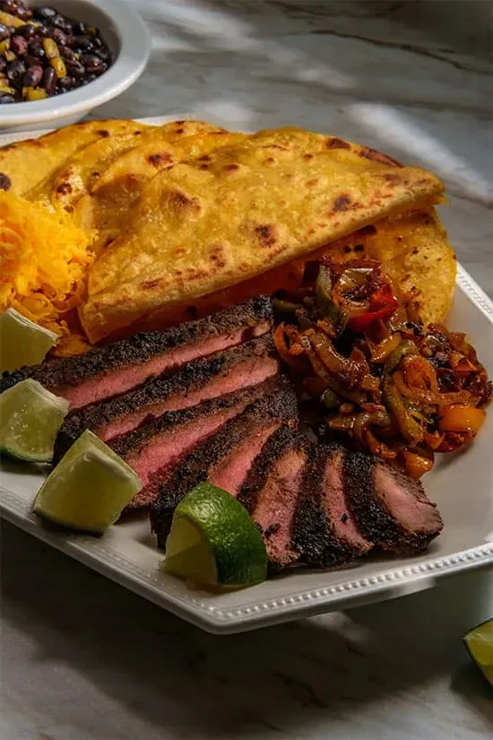 Plated steak fajitas with tortillas, cheese, lime, and peppers.