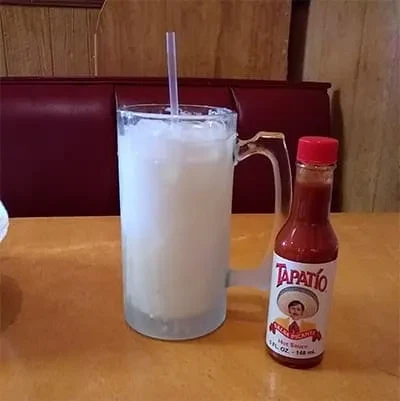 Mug with milky drink and straw, beside Tapatío hot sauce bottle.