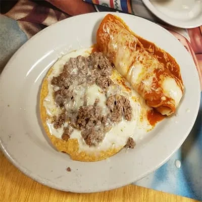 Plate with a meat tostada and a red enchilada, cheese-topped.