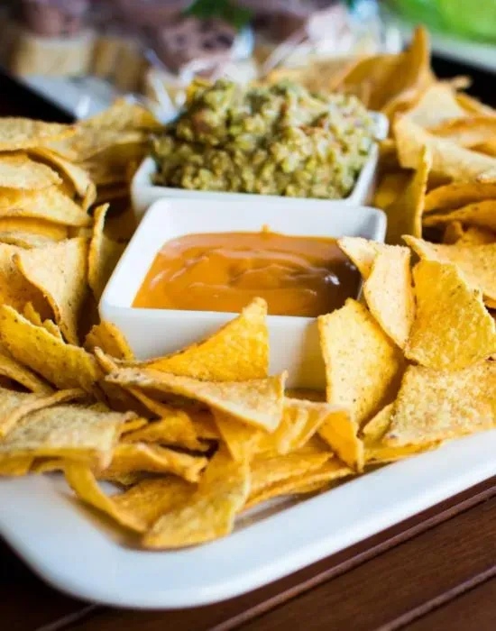 Nachos with orange queso and green guacamole on a white platter.