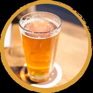 Pint glass of amber beer with foam on wood, rustic border.