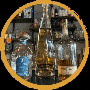 Three distinct spirit bottles: blue, tall, wide, on a bar.