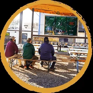 Three men watch a football game on a large outdoor screen.