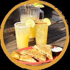 Quesadillas, dipping sauce, and iced lime drinks on rustic wood.