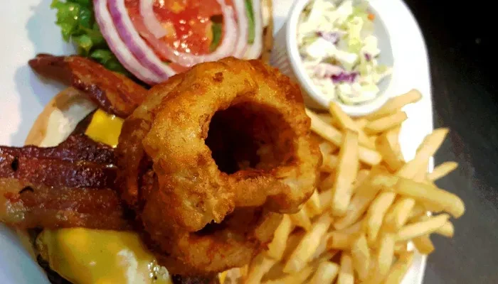 Burger topped with onion rings, fries, and coleslaw on a plate.