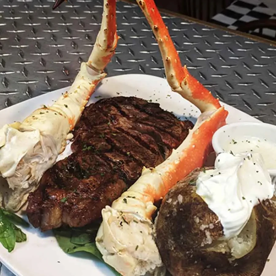 Steak, crab legs, and baked potato with sour cream and chives.