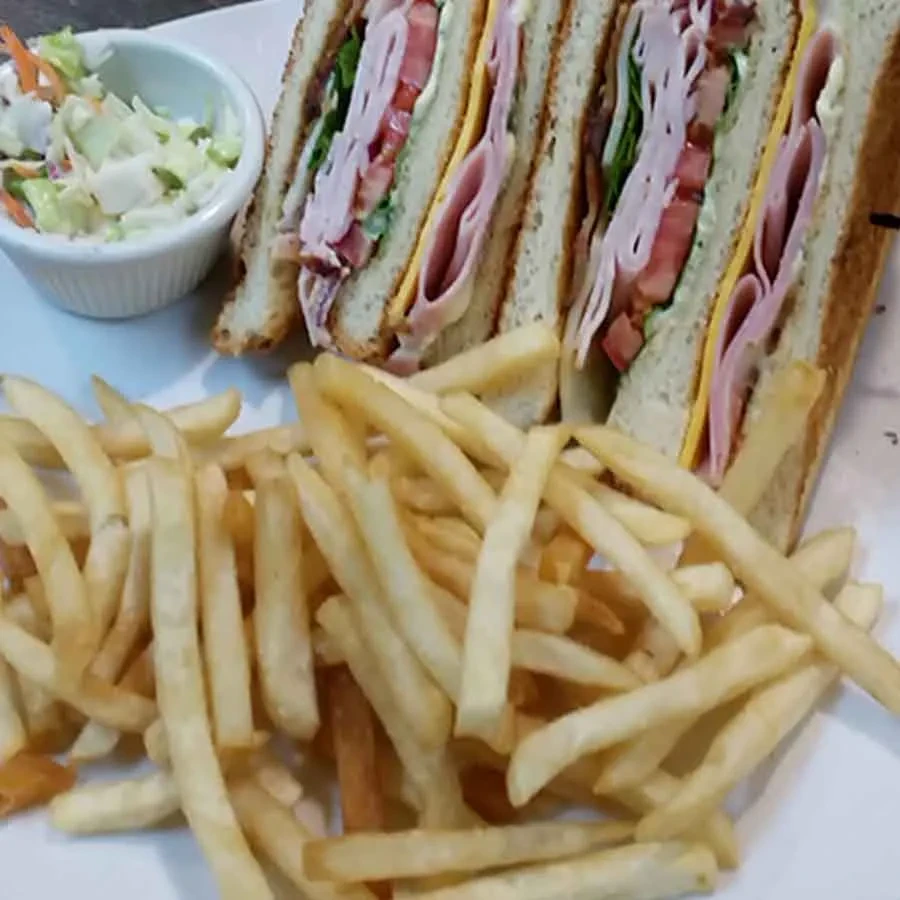 Club sandwich, french fries, and coleslaw on a white plate.