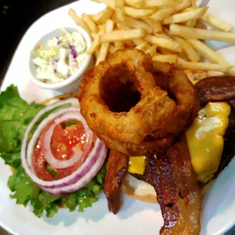 Diner-style burger with bacon, onion rings, fries, and coleslaw.