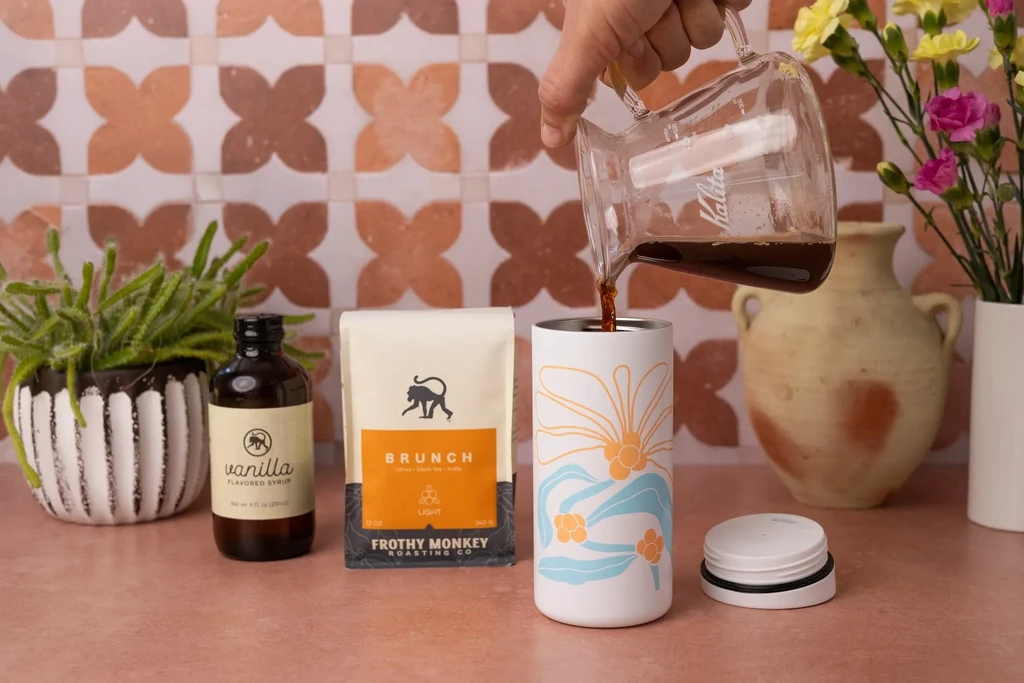 Hand pouring dark coffee from Kalita into a floral tumbler.