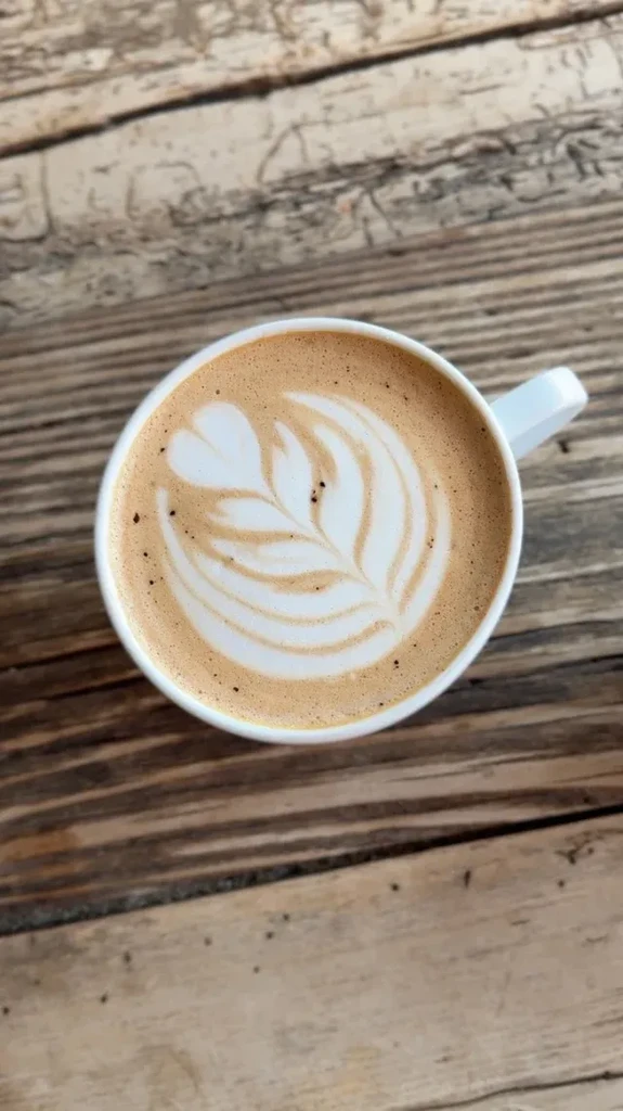 Top-down white mug with rosetta latte art on rustic wood.