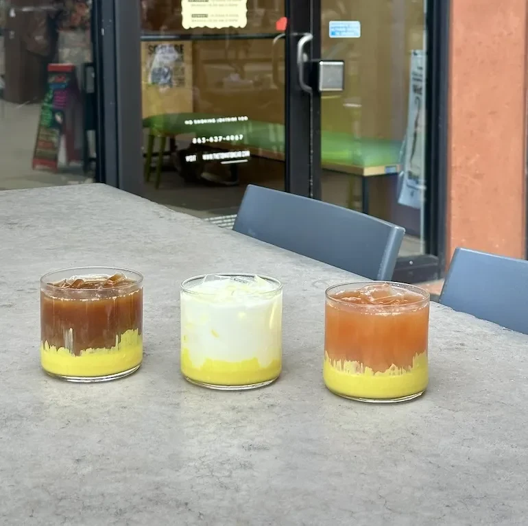 Three colorful layered drinks on a gray table, cafe background.
