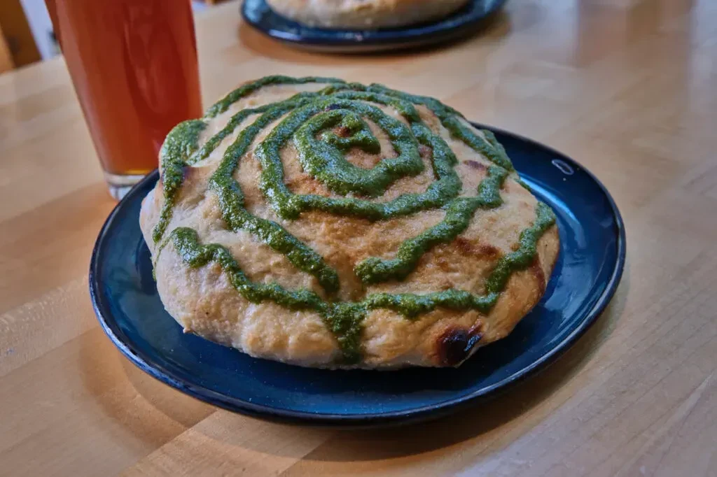 Close-up of focaccia with green pesto swirl on a blue plate.