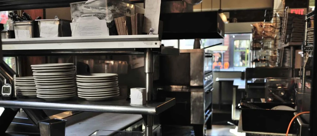 Organized commercial kitchen shelves holding plates, cutlery, and a timer.