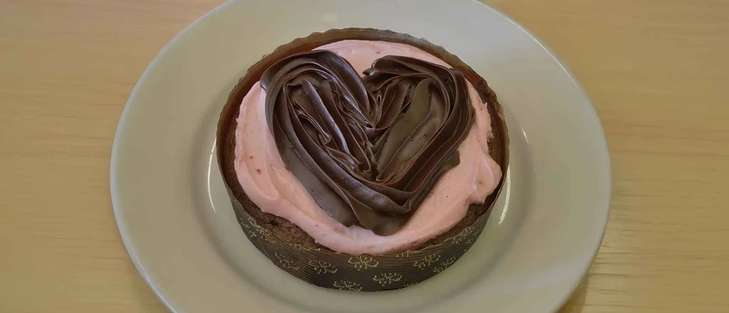 Chocolate cake with pink frosting and a decorative chocolate heart.