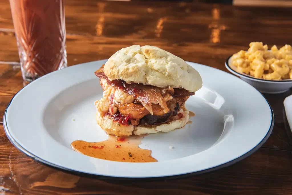 Biscuit sandwich with fried chicken, eggs, and red jam on a plate.