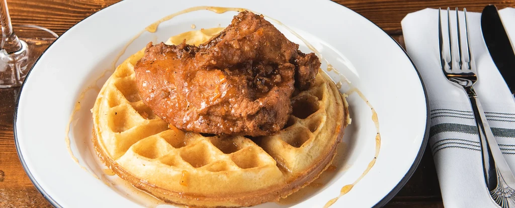 Top-down: fried chicken and waffles with syrup on enamelware plate.