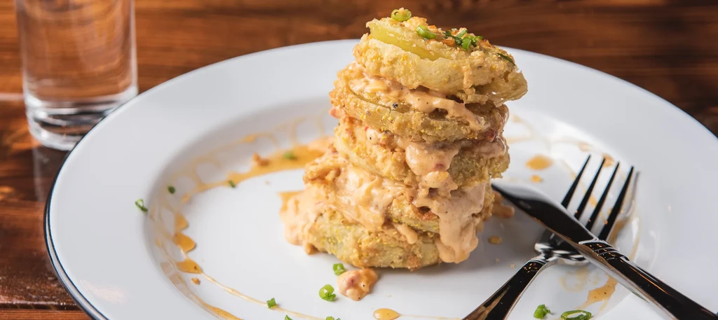 Stack of fried green tomatoes, creamy orange sauce, green onions on a white plate.