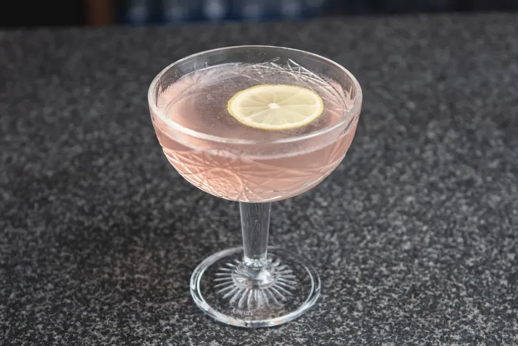 Effervescent pale pink cocktail with citrus slice in etched coupe glass.