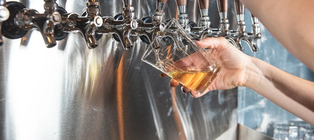 Hand pouring golden beer from chrome tap into faceted glass.